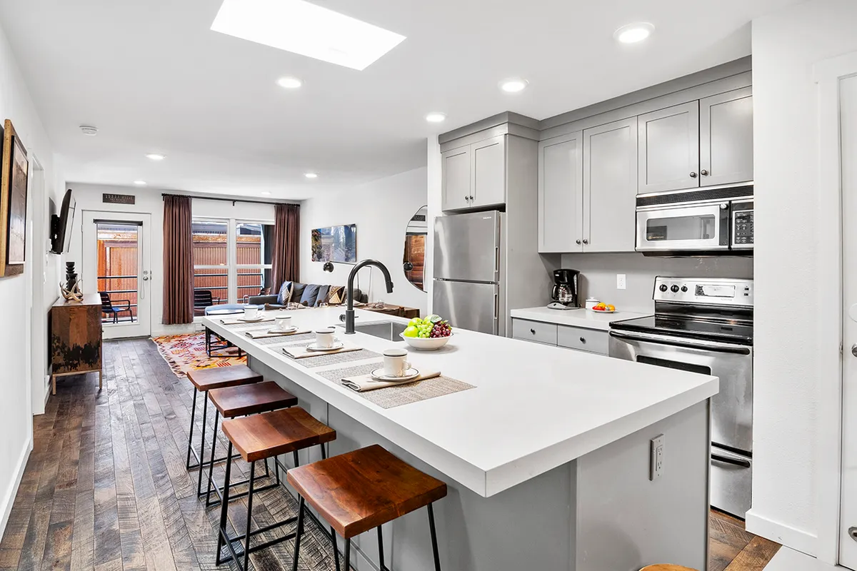 A spacious, modern kitchen featuring a central island with stylish stools, sleek appliances, ample cabinetry, and a well-set dining area—perfect for preparing and enjoying meals. The space is designed for both casual brunches and festive gatherings, exuding a welcoming and contemporary ambiance.