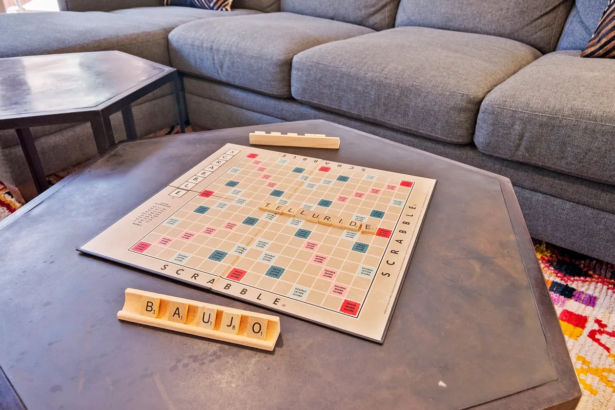 A playful, relaxed living area featuring a Scrabble board on the coffee table, surrounded by a comfortable sectional couch. The setup is perfect for game nights, showcasing a casual and inviting vibe, with soft lighting and a focus on communal fun.