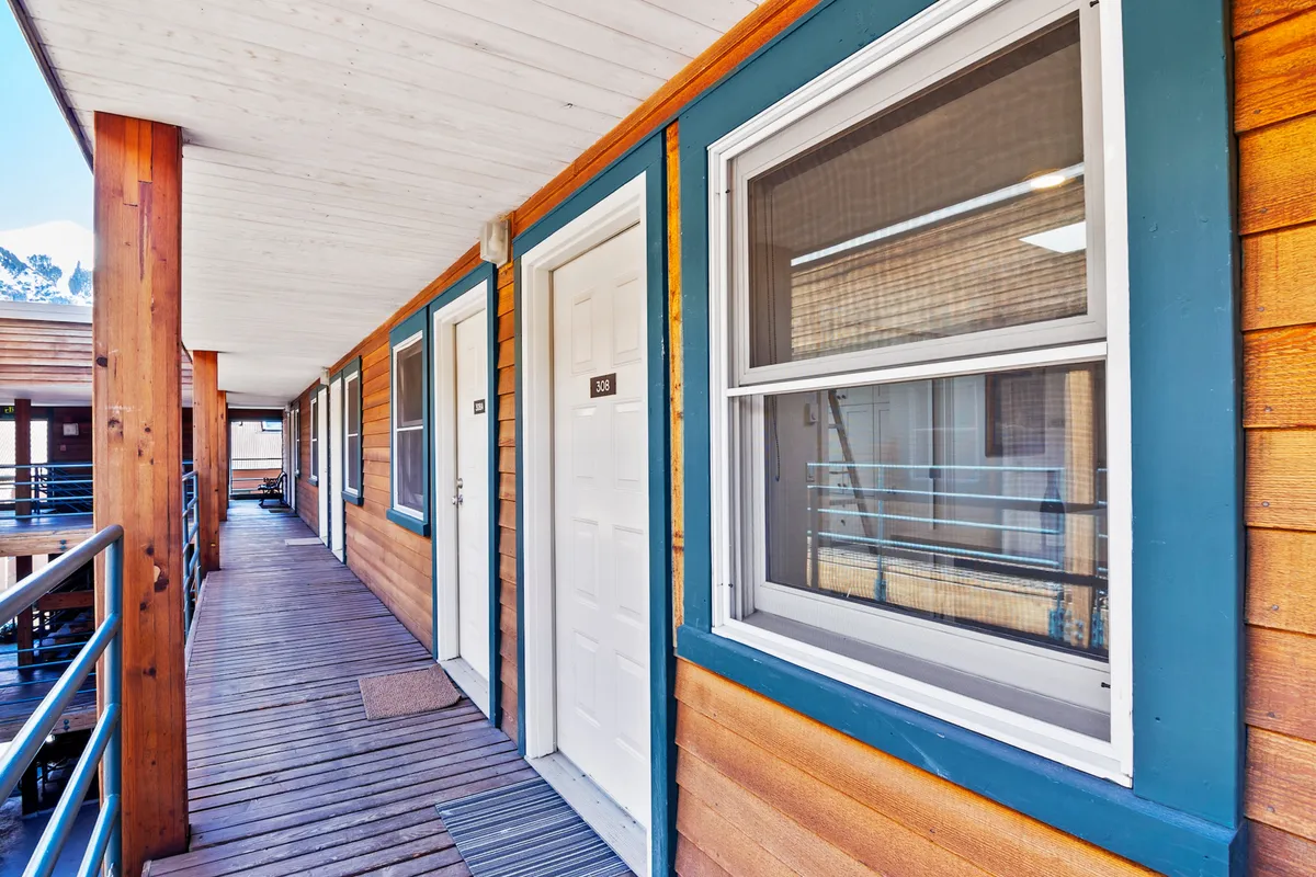 An exterior view of a residential building with wooden paneling, white doors, and a balcony railing. The scene evokes relaxation, social interactions on the porch, and enjoying the surrounding views—ideal for winding down after lively events.