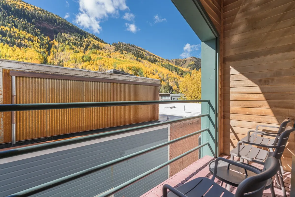 A serene balcony with comfortable seating overlooks golden autumn trees and dramatic mountain vistas. The view invites relaxation after a day’s adventure, highlighting the personal connection to the outdoors from the condo itself.
