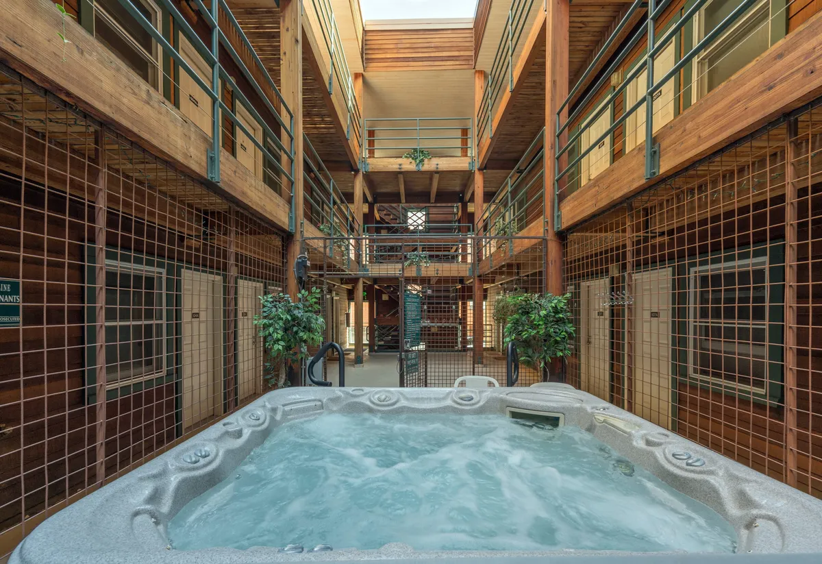 This image showcases the HOA-managed communal hot tub nestled among wooden structures and green plants, with balconies visible above. People are seen relaxing in the hot tub, giving a sense of community and post-adventure relaxation.