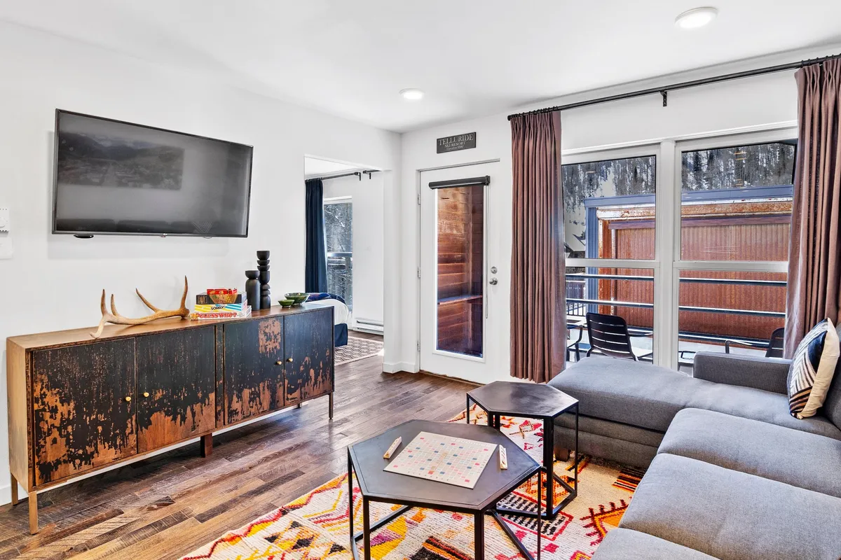 A cozy living room scene with a sofa facing a television, a coffee table, side table, and curtains. The layout encourages relaxation—watching TV, playing games, or simply enjoying each other's company.