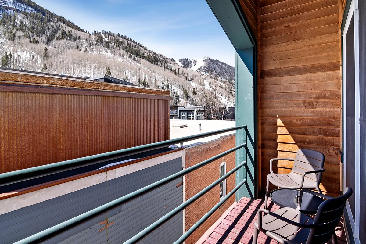 A tranquil private balcony with comfortable seating, wooden architectural details, and sweeping mountain views. The space invites relaxation with a cup of coffee or a glass of wine, directly connecting the indoor kitchen to the stunning outdoor environment.